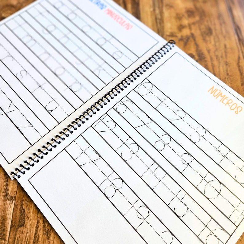 May include: A spiral-bound educational workbook featuring white pages with black dashed lines for tracing lowercase letters and numbers. The left page displays the alphabet, while the right page shows the text N&Uacute;MEROS and rows of numbers for practice.