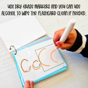 May include: A child's hand uses a dry-erase marker to trace the letter "C" on a white flashcard with a black dotted outline. The flashcard is part of a colorful binder with a silver ring.