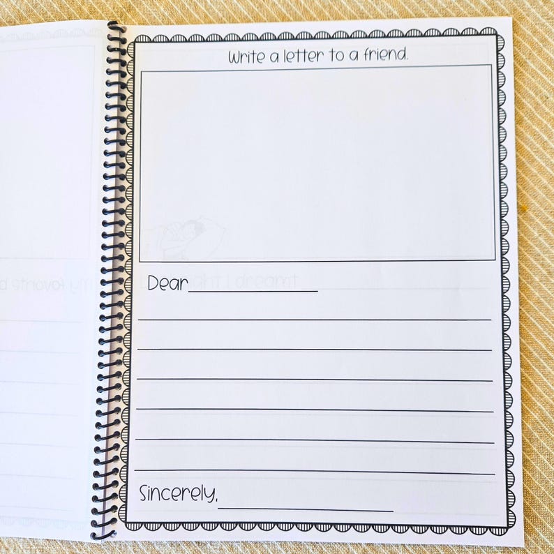 May include: Open notebook with lined pages and a spiral binding. The page features the text "Write a letter to a friend" at the top, with space for a drawing and lines for writing. The notebook is open on a light-colored surface.
