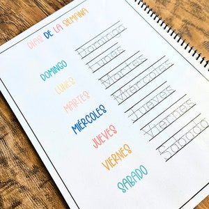 May include: A spiral-bound educational worksheet titled D&Iacute;AS DE LA SEMANA featuring a list of the days of the week in Spanish. The page includes colorful printed text and corresponding dotted-line words for tracing practice in black ink.