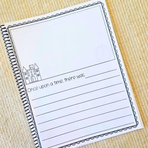 May include: A spiral-bound notebook with a white cover featuring a black border and the text "Once upon a time, there was". The notebook has a castle illustration and lined pages for writing.