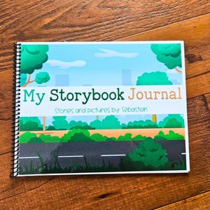 Może przedstawiać: Szyty spiralnie dziennik z kolorową okładką przedstawiającą scenę miejską z drzewami, drogą i tekstem "My Storybook Journal" oraz "Stories and pictures by: Sebastian".