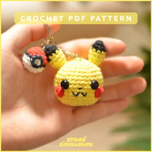 Può includere: Un portachiavi Pikachu all'uncinetto giallo con occhi neri, guance rosse e orecchie con la punta nera. È attaccata una piccola Poké Ball all'uncinetto. Il testo "CROCHET PDF PATTERN" è in alto.