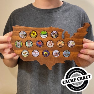 May include: A wooden United States map with 18 round, colorful, metal geocaching trackable coins displayed in the outline of the country. The map is labeled "CACHE CRAFT" with a website address.
