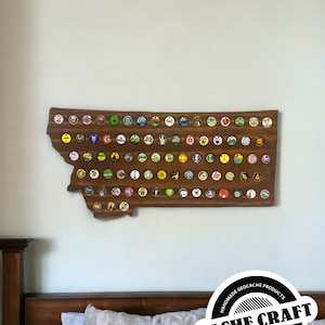 May include: A wooden outline of the state of Montana with a collection of colorful geocaching trackable tags attached. The wooden outline is mounted on a wall. The text "HANDMADE GEOCACHE PRODUCTS CACHE CRAFT WWW.CACHECRAFTNJ.COM" is on a black and white circle.