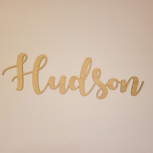 May include: A wooden sign with the name "Hudson" written in cursive script.