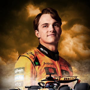 Puede incluir: Un piloto de Fórmula 1 que lleva un traje de carreras negro y naranja con la palabra "Android" en el pecho. El piloto está de pie frente a un coche de carreras de Fórmula 1 negro y naranja con las palabras "Oscar Piastri" impresas debajo del coche.