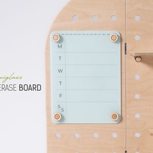 May include: A light blue dry erase board with a weekly calendar layout. The board is made of plexiglass and has four wooden knobs on the corners. The board is mounted on a wooden pegboard with white dots.