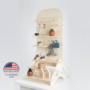 May include: A white wooden display stand with four shelves and a small step stool. The stand is decorated with a variety of items, including a potted plant, a ceramic mug, and a macrame wall hanging. The stand is ideal for displaying small items, such as jewellery, crafts, or other small goods.