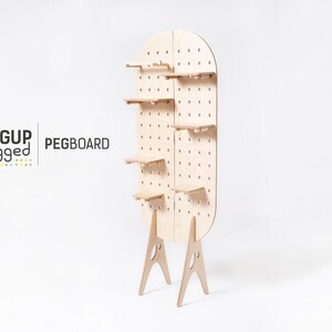 May include: A freestanding pegboard with five shelves and a rounded top. The pegboard is made of light wood and has a grid of holes for hanging items. The pegboard is supported by two A-shaped legs.
