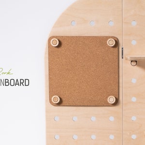 May include: A light wood pinboard with a cork board section. The cork board is surrounded by a light wood frame and has four small wooden knobs in the corners. The pinboard has a grid of holes for hanging items.