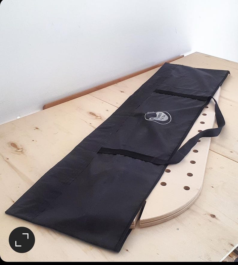 May include: A black canvas bag with a zipper and a handle. The bag is lying on a light wood surface. The bag has a white logo that says "Rock Solid" on it.