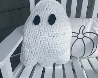May include: White crocheted ghost cushion with black eyes. The cushion is sitting on a white wooden rocking chair.