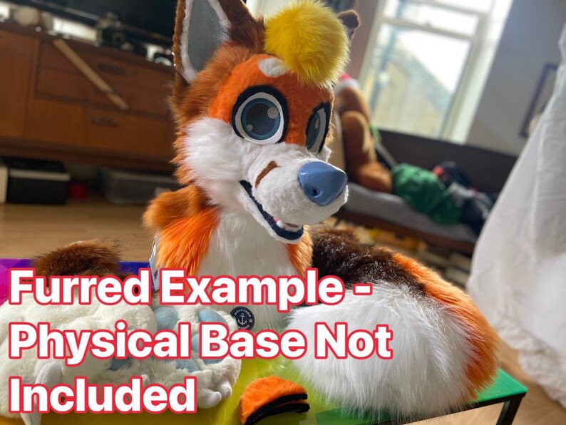 May include: A furry orange, white and brown fox head with a yellow pom-pom on top. The head is sitting on a table with a green surface. The text "Furred Example - Physical Base Not Included" is visible in the image.