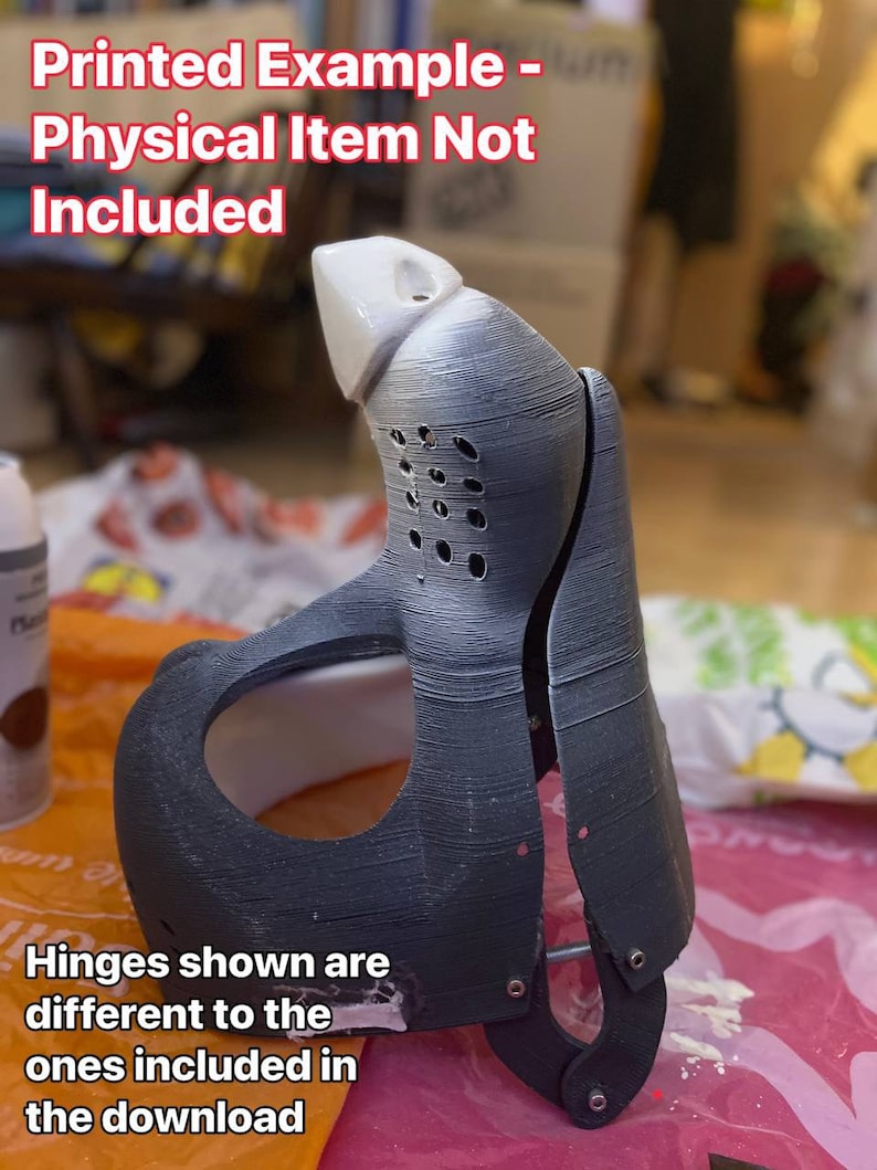 May include: A 3D printed example of a black and white mask with hinges. The text "Printed Example - Physical Item Not Included" is at the top of the image. The text "Hinges shown are different to the ones included in the download" is at the bottom of the image.