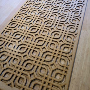 May include: A rectangular wooden panel featuring a repeating geometric pattern. The panel is light brown with dark brown cut-out details, creating a layered effect. The design is intricate and symmetrical, suitable for decorative use.