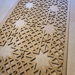May include: A wooden decorative panel featuring a geometric design of interlocked triangles and squares. The panel is crafted from light brown wood and has a natural finish.