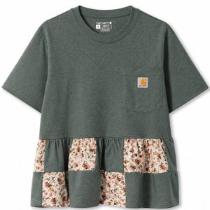 Puede incluir: Camiseta verde de manga corta con bolsillo y diseño patchwork floral en la parte inferior. La camiseta tiene un corte holgado y un pequeño parche con el logo en el bolsillo.