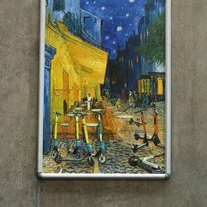 Könnte beinhalten: Ein gerahmter Druck eines Gemäldes, das eine Nachtszene mit einem gelben Gebäude und einem sternenklaren Himmel darstellt. Das Gemälde zeigt mehrere Personen, die auf der Straße gehen, und eine Gruppe von Elektro-Rollern, die vor dem Gebäude geparkt sind.