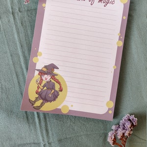 May include: A purple notepad with a witch illustration and the text "Just a touch of magic". The notepad has yellow polka dots and lined paper.