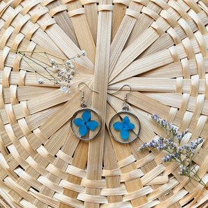 May include: A pair of silver hoop earrings with a blue pressed flower inside each hoop.