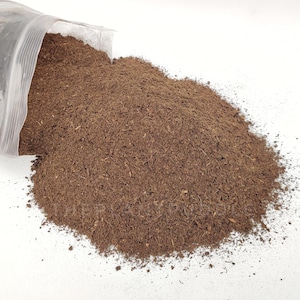 Peut inclure: Gros plan sur un matériau brun, lâche et fibreux, probablement un type de terre ou de compost, qui se répand d'un sac en plastique transparent sur une surface blanche.