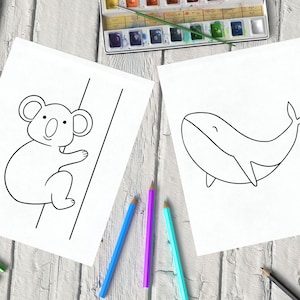 Two coloring pages with simple line drawings of a koala and a whale, on a wooden surface surrounded by colored pencils and watercolors.