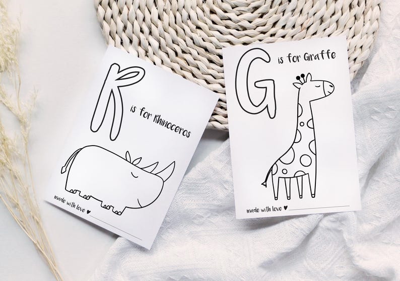 May include: Two white cards with black line drawings of animals and letters. One card says "K is for Rhinoceros" with a rhino illustration. The other says "G is for Giraffe" with a giraffe illustration. Both cards say "made with love".