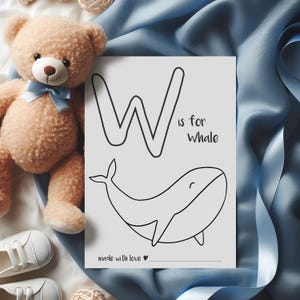 May include: A beige teddy bear with a blue bow sits next to a white card with a black outline of the letter "W" and a whale illustration. The text "W is for Whale" and "made with love" are also on the card. White baby shoes are in the image.