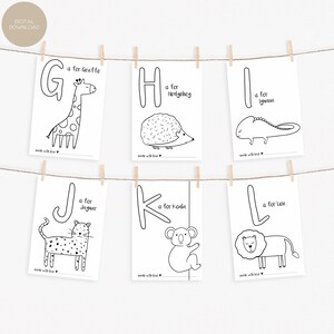 May include: Six black and white alphabet cards with animal illustrations, including a giraffe, hedgehog, iguana, jaguar, koala, and lion. Each card features a large letter and the animal's name. The cards are hanging from a string with wooden clips.