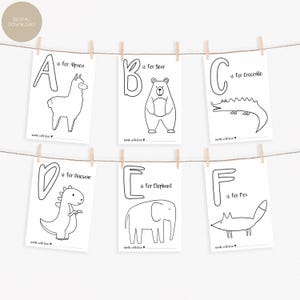 May include: Six black and white alphabet flashcards are displayed, each featuring a letter and an animal illustration. The cards are suspended from a string with wooden clothespins. The letters A through F are shown, with animals like an alpaca, bear, crocodile, dinosaur, elephant, and fox.
