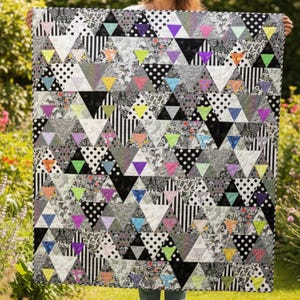 Puede incluir: Un edredón geométrico con un diseño de patchwork de triángulos en varios patrones y colores. El edredón incorpora lunares blancos y negros, rayas y estampados florales, con acentos de triángulos amarillos, rosas, morados y verdes.