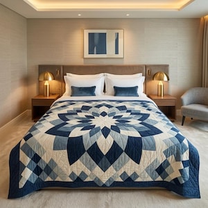 May include: A bed with a blue and white geometric patterned quilt. The quilt features a large floral design in shades of blue and white. The bed is made with white pillows and blue velvet accent pillows. Two gold lamps sit on wooden nightstands.