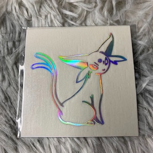 Peut inclure: Autocollant holographique représentant une créature de dessin animé stylisée avec de grandes oreilles et une longue queue. L'autocollant a un éclat arc-en-ciel, avec des couleurs changeant avec la lumière. L'autocollant est sur fond blanc et scellé dans une pochette plastique transparente.