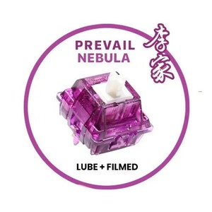 May include: A purple mechanical keyboard switch with a white stem. The switch is labeled "Prevail Nebula" and "Lube + Filmed".