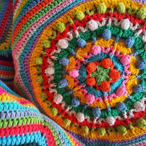 Könnte beinhalten: Ein farbenfrohes gehäkeltes Kissen mit einem runden Design, das eine Vielzahl von Farben aufweist, darunter Rot, Orange, Gelb, Grün, Blau und Pink. Das Kissen hat eine strukturierte Oberfläche und ist mit verschiedenen Maschen gearbeitet.