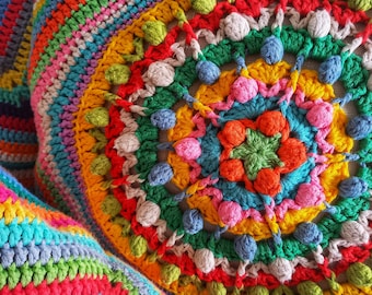 Peut inclure: Un coussin crocheté coloré avec un motif circulaire présentant une variété de couleurs, notamment le rouge, l'orange, le jaune, le vert, le bleu et le rose. Le coussin a une surface texturée et est réalisé avec une variété de points.
