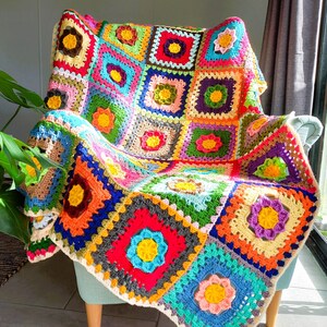 May include: A colorful crocheted throw blanket with a floral pattern, draped over a light blue armchair. The blanket is made of squares in various colors, including red, orange, yellow, green, blue, and purple.