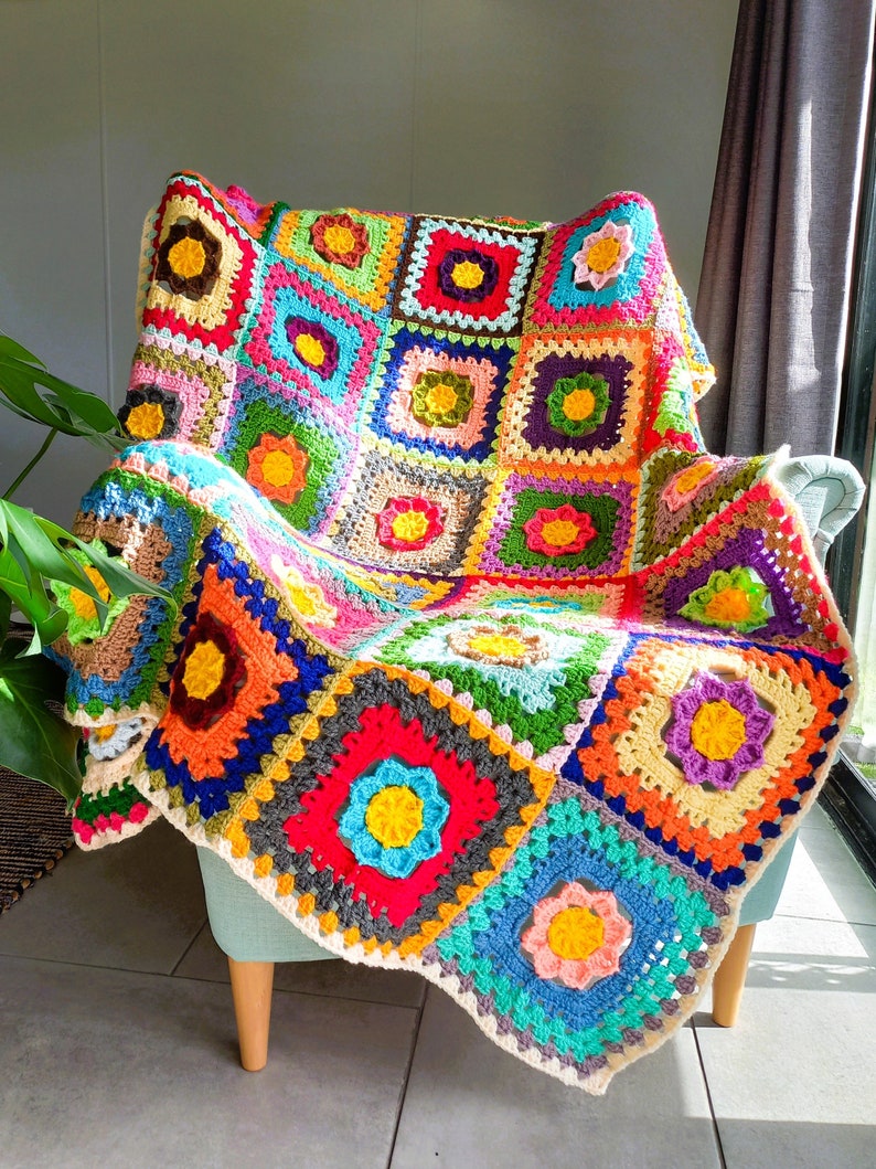 May include: A colorful crocheted throw blanket with a floral pattern, draped over a light blue armchair. The blanket is made of squares in various colors, including red, orange, yellow, green, blue, and purple.