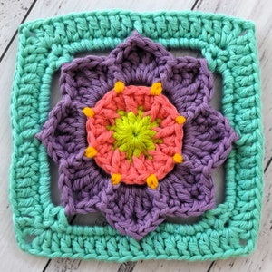 May include: A crocheted square with a purple flower in the center. The flower has a pink and yellow center and is surrounded by a teal border.