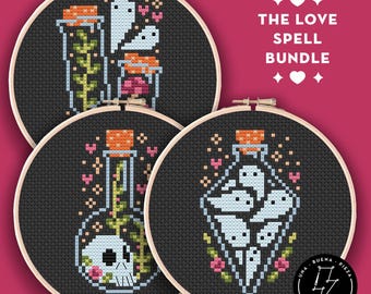 May include: Three circular wooden embroidery hoops containing black fabric with cross-stitch designs of glass bottles, ghosts, skulls, plants, and hearts. The text THE LOVE SPELL BUNDLE is printed in white with heart icons above and below.