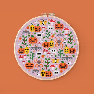 May include: A purple and white cross-stitch embroidery hoop with a Halloween-themed design. The design features pumpkins, bats, ghosts, spiders, and mushrooms.