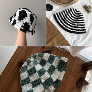 Può includere: Tre cappelli a secchiello all'uncinetto con diversi motivi. Uno presenta una stampa a mucca bianca e nera, un altro ha strisce bianche e nere e il terzo un motivo a scacchiera verde e bianco. I cappelli sono fatti a mano.