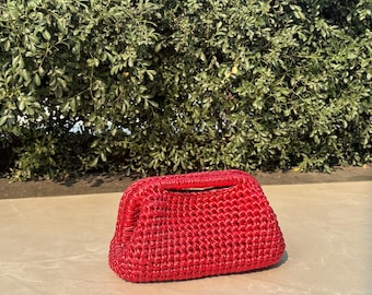 May include: A bright red, hand-crocheted clutch bag featuring a structured, rectangular frame with a top opening. The exterior is crafted from a thick, glossy cord material with a consistent, dense woven texture throughout the entire body.