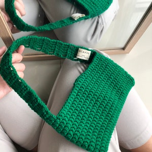Op de afbeelding: Een groene gehaakte handtas met een klein label met de tekst "OCAVVE 2020 HANDMADE CROCHET".