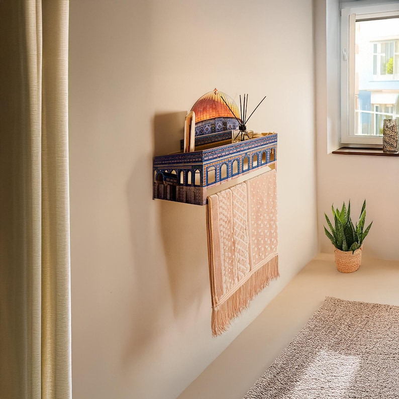 Pu&ograve; includere: Mensola da parete decorativa con un design architettonico dettagliato, con una cupola e finestre ad arco. La mensola &egrave; dipinta nei toni del blu, marrone e arancione. Un asciugamano rosa con frange &egrave; appeso sotto. Un diffusore a lamelle e un libro sono sulla mensola.