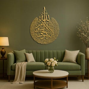 May include: A gold-colored, circular wall art piece featuring Arabic calligraphy. The artwork is mounted on a green wall above a green sofa. The room is decorated with a lamp, coffee table, and vase of flowers, creating a warm and inviting atmosphere.
