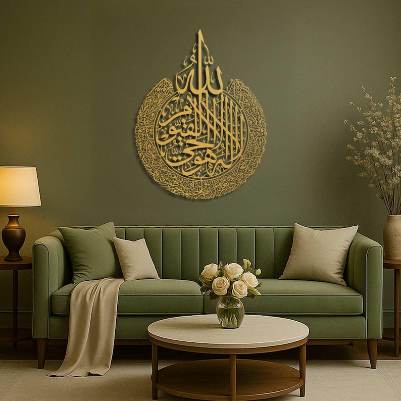 May include: A gold-colored, circular wall art piece featuring Arabic calligraphy. The artwork is mounted on a green wall above a green sofa. The room is decorated with a lamp, coffee table, and vase of flowers, creating a warm and inviting atmosphere.