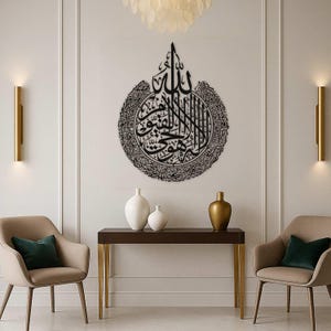 May include: A large, black metal wall art piece featuring Arabic calligraphy. The artwork is circular with intricate details and is mounted on a white wall. The room is decorated with modern furniture and lighting.