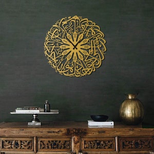 May include: A gold-colored, circular wall clock featuring intricate Arabic calligraphy. The clock hands are black, and the design is mounted on a dark green wall. The clock is a decorative piece, adding a touch of elegance to any room.